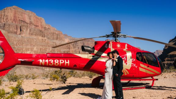a couple embrace during their wedding at the Grand Canyon with a helicopter tour landed next to them