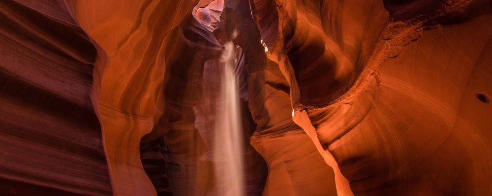A shaft of sunlight shines down to the floor of Antelope Canyon