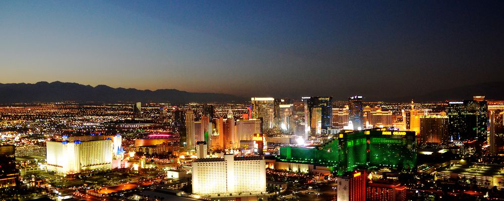 Strip casinos illuminated by neon lights while the sun sets behind nearby mountains
