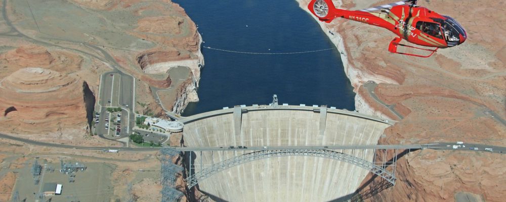 Red helicopter flying over Glen Canyon Dam during an aerial tour.
