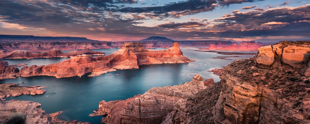 Lake Powell and surrounding rock formations beneath a pink and purple sunset