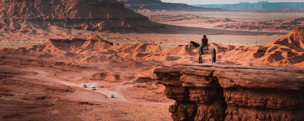 Two people stand atop a stone cliff overlooking the Navajo desert landscape
