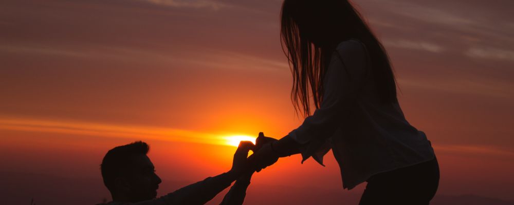 a silhouette of a man proposing to a woman in front of sunset