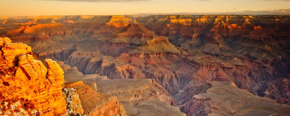 A golden sunset casts light across a vast wall of the Grand Canyon South Rim