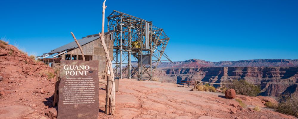 a sign designating Guano Point at the grand canyon west with an old mining structure in the background