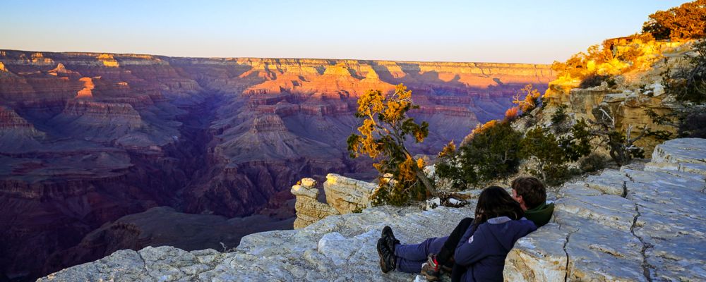 A couple rests at the edge of the Grand Canyon watching the sunset