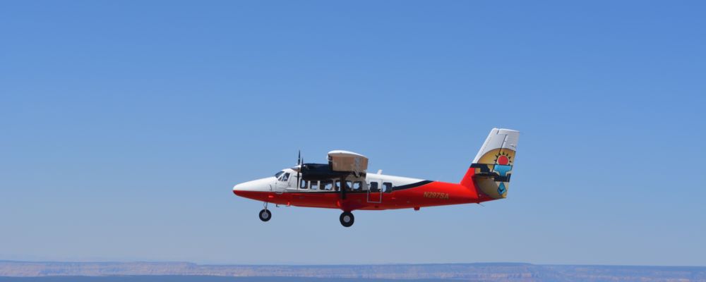 Red and white Twin Otter Airplane on an aerial tour with a blue sky.