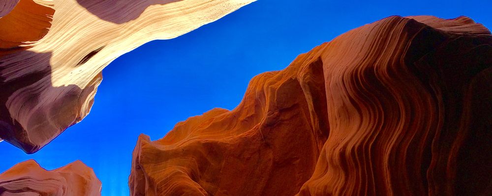 An upward view of Antelope Canyon's walls with a blue sky peeking through