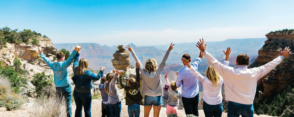 A family stands at the edge of the Grand Canyon with their arms raised in the air