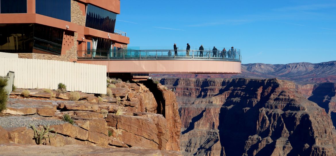 Grand Canyon Skywalk guests at the Grand Canyon West stand atop the Skywalk bridge surrounded by canyon scenery