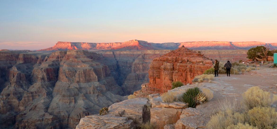 two people stand at the edge of the grand canyon at sunset