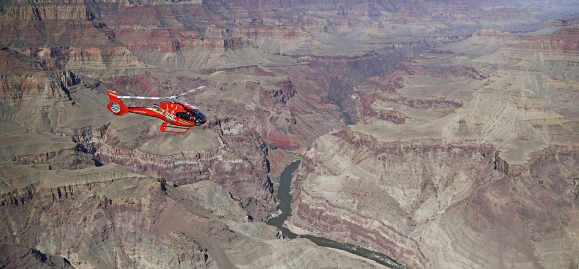 A red helicopter flies over the expanse of the Grand Canyon National Park