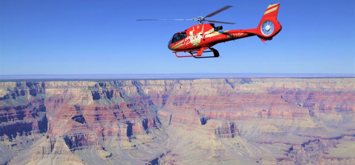 a red helicopter flies over the Grand Canyon gorge