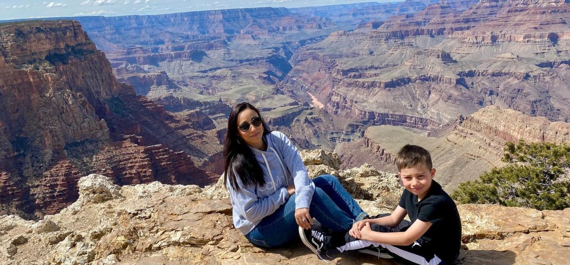 A mother and son pose sitting at the edge of a Grand Canyon National Park lookout point