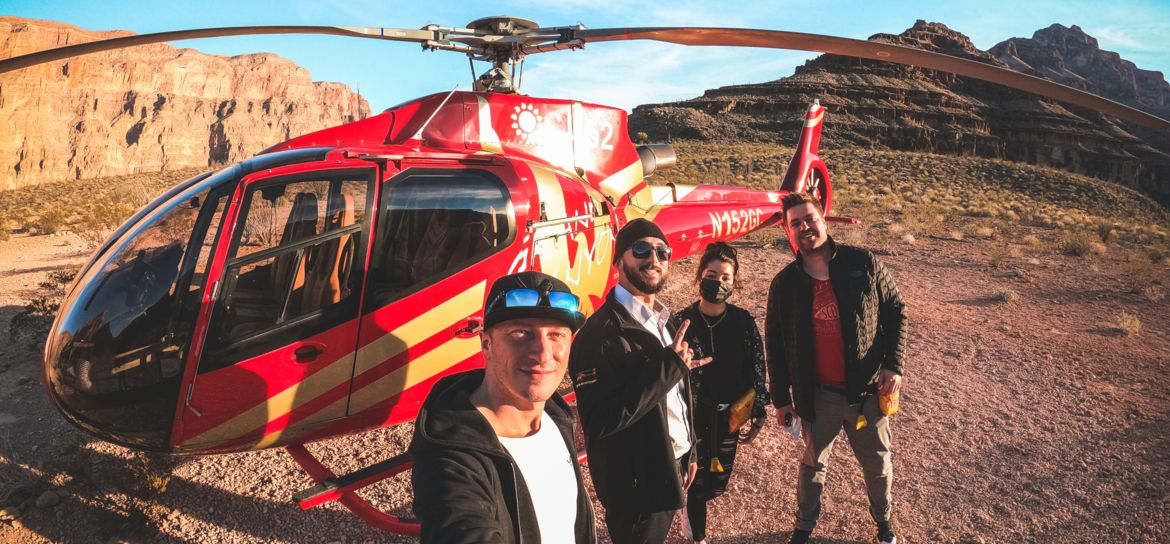a group of men pose for a selfie in front of a helicopter at the bottom of the Grand Canyon West
