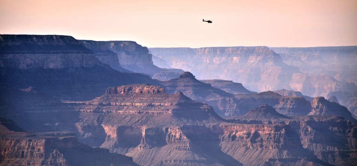 a broad shot of Grand Canyon scenery where a silhouette of a helicopter flies far away in the sky