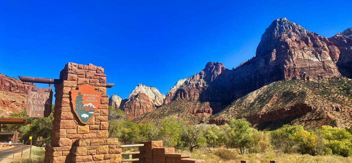 Zion National Park entrance the entrance sign outside Zion National Park with the massive canyon walls in the background