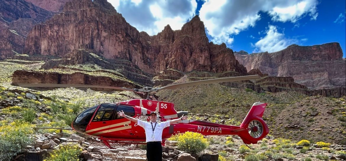 a Grand canyon helicopter tour landed on the very bottom of the West Rim; pilot stands in front of aircraft.