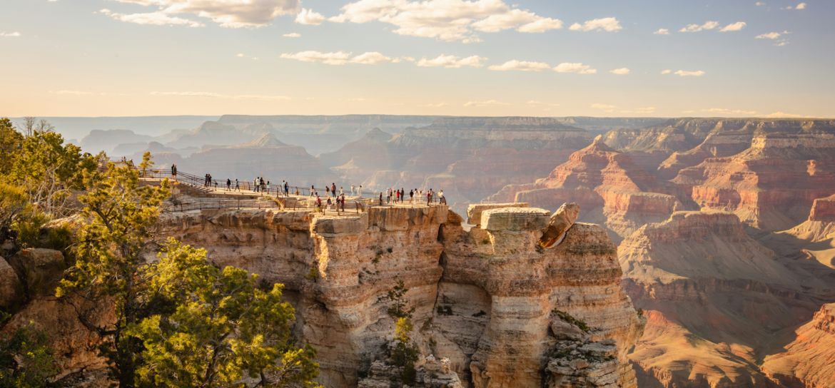 several visitors to the Grand Canyon National Park stand atop a stunning lookout point overlooking the landscape