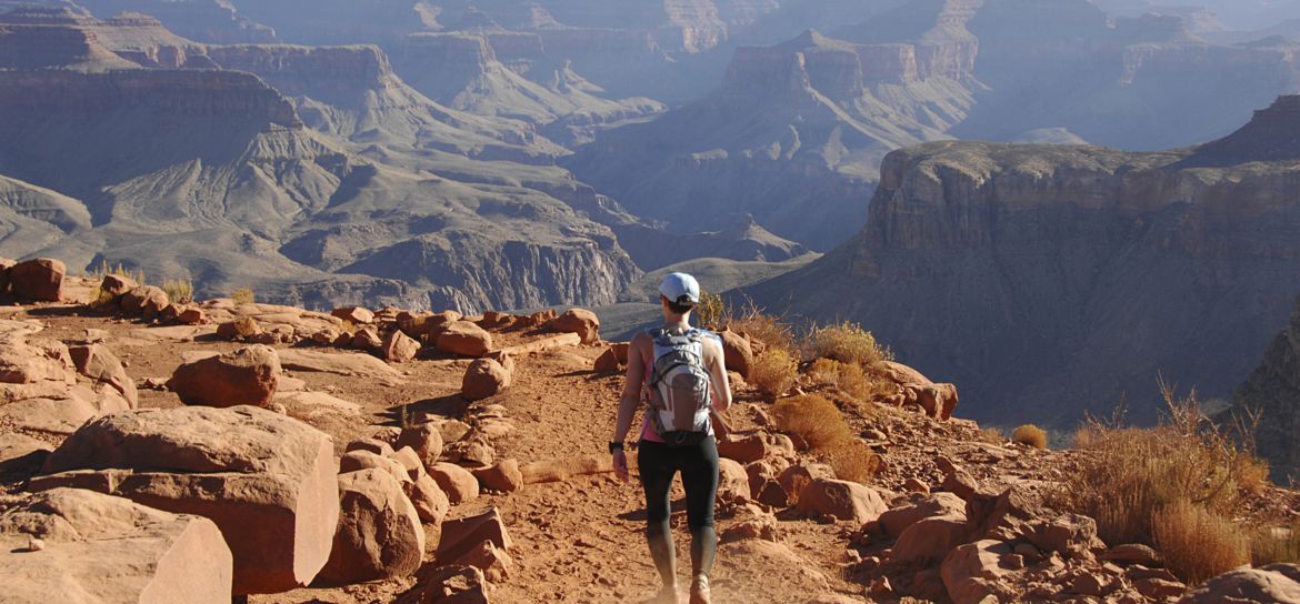 a female hiker walks with her back facing the camera along a Grand Canyon trail
