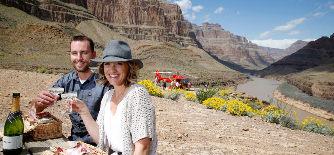 a couple smile while sitting at a picnic table after landing on the bottom of the Grand Canyon West
