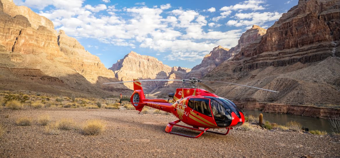 a red helicopter landed at the very bottom of the Grand Canyon West with canyon walls seen on either side