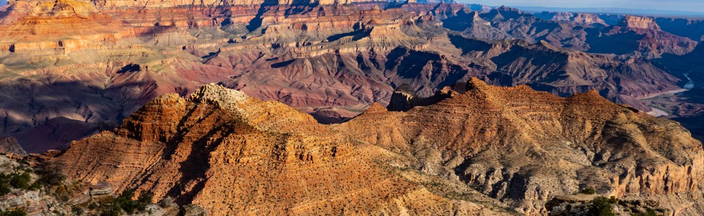 a Grand canyon landscape featuring a colossal sandstone wall illuminated by the desert sunset