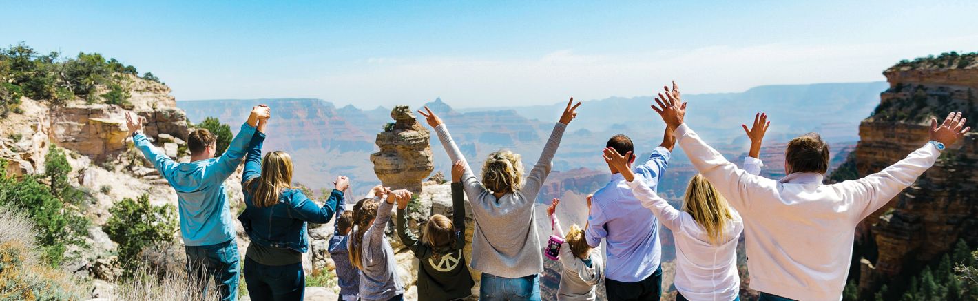 a family stands at a Grand Canyon National Park viewpoint with their arms in the air