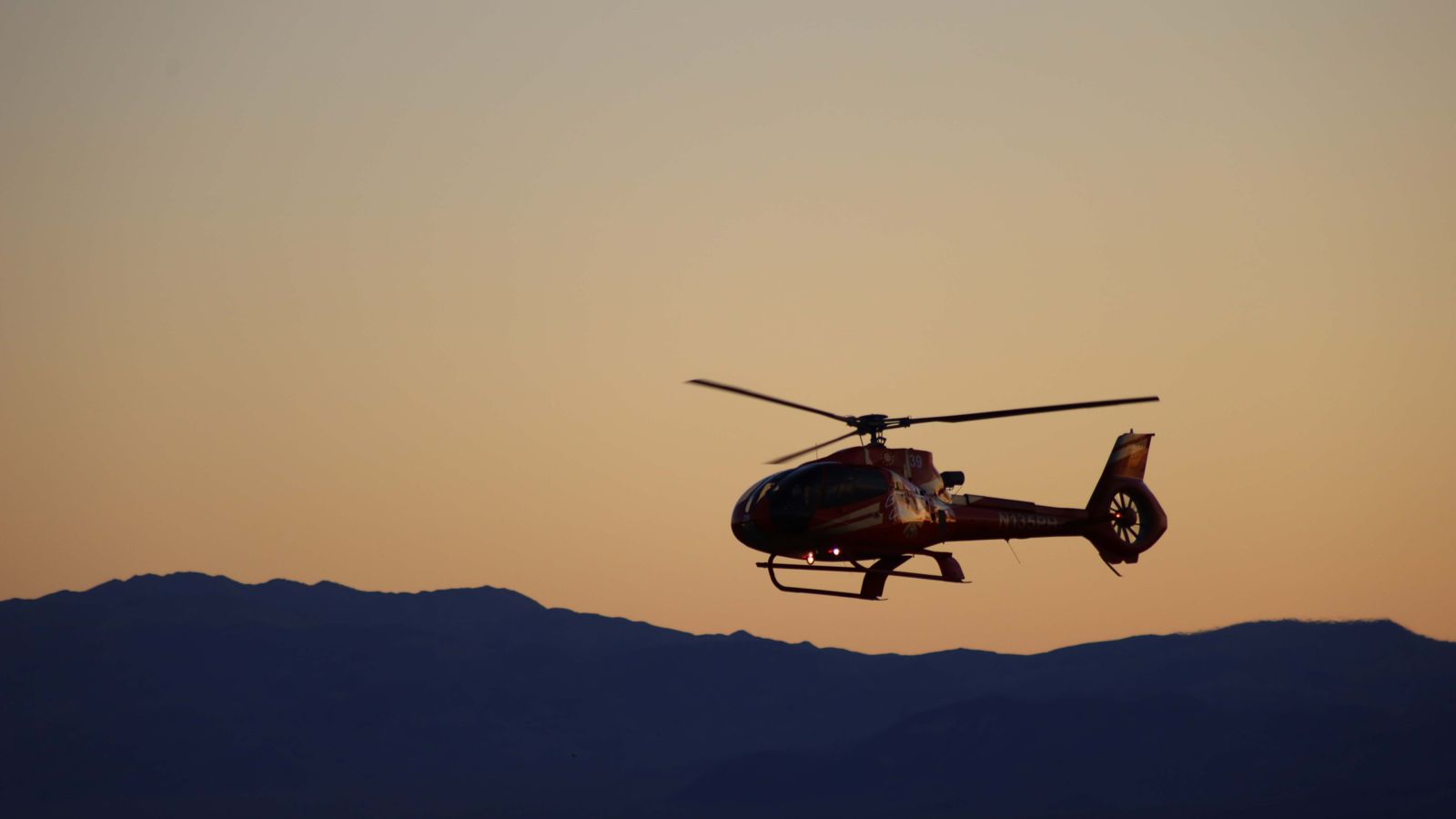 A helicopter flying in the air during sunset with a mountain range in the background.
