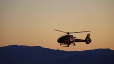 A helicopter flying in the air during sunset with a mountain range in the background.