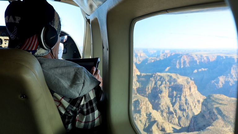 A man aboard a Grand Canyon airplane tour takes a photo of the landscape through his window using his phone.