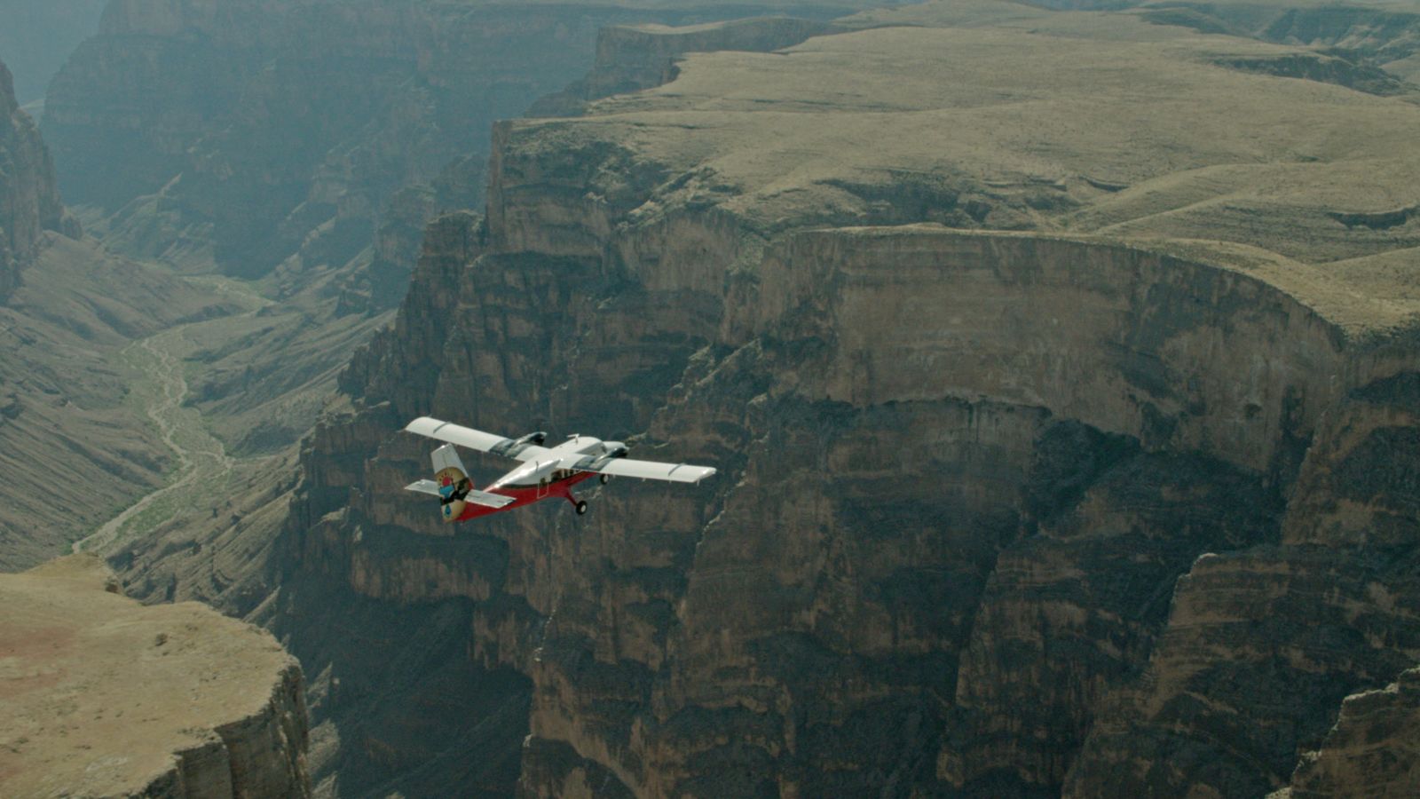 A red and white airplane flying over the Grand Canyon West.