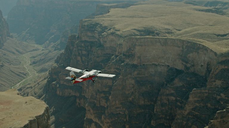 A red and white airplane flies over a huge stone gorge within the Grand Canyon West.