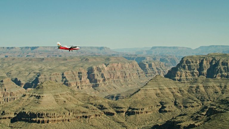  A small red and white airplane soars over a stone gorge of the Grand Canyon West Rim.