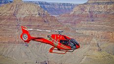 A red helicopter flying over the Grand Canyon.