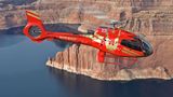 A red helicopter flies through the walls of the Grand Canyon above the Colorado River.