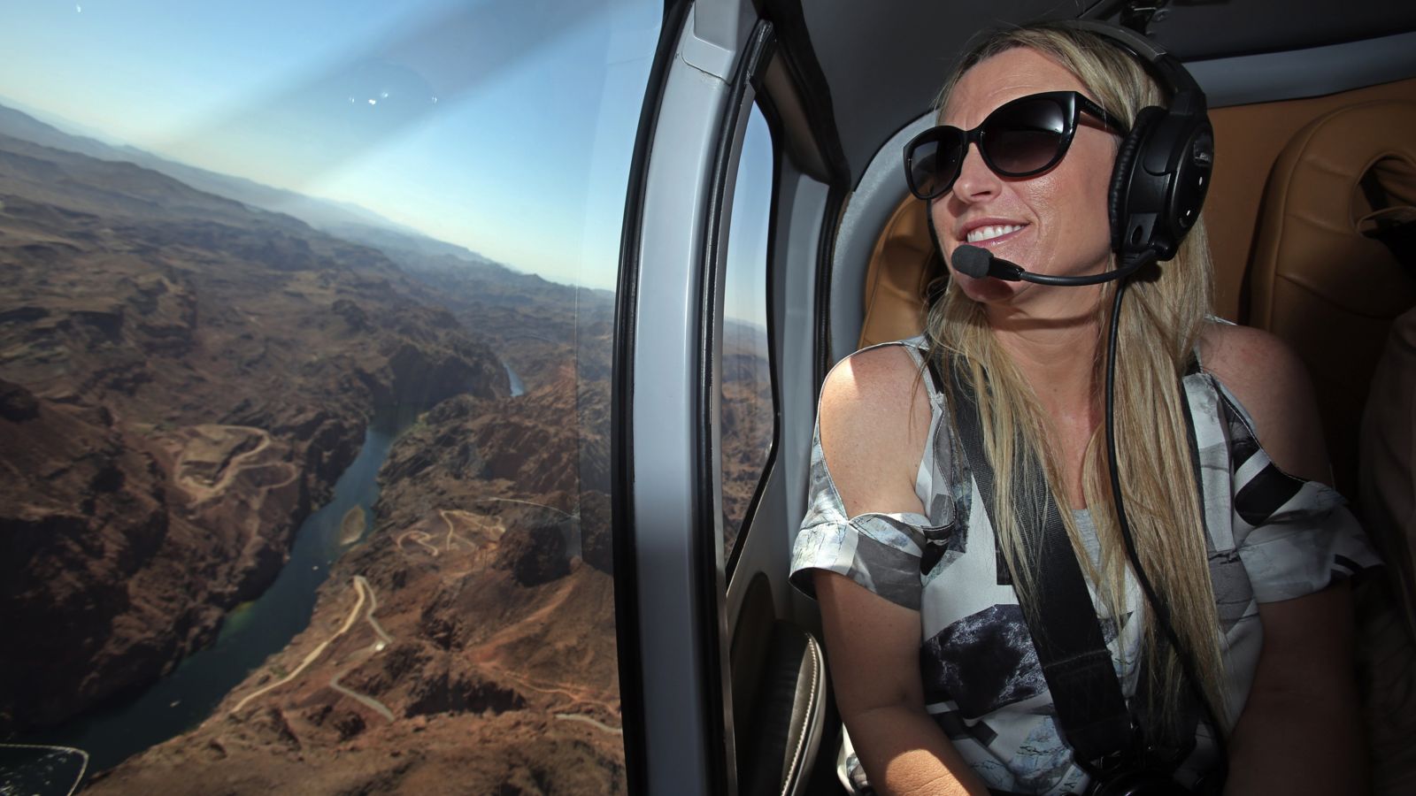 a female passenger smiles looking out the window of a Las Vegas helicopter tour flying over the Colorado River