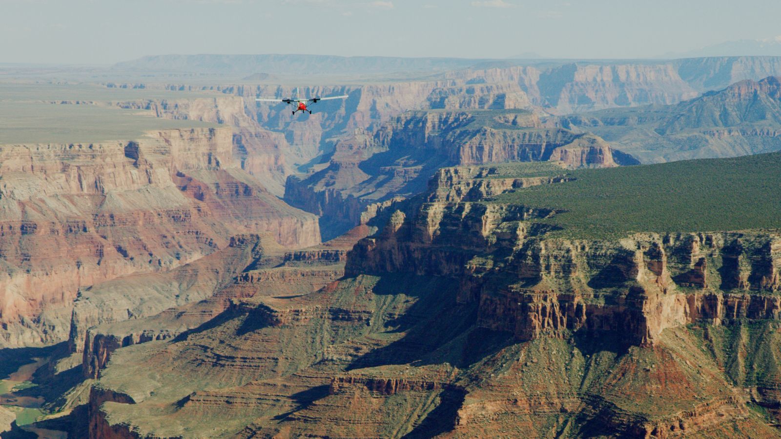 A sightseeing airplane seen in the distance flying over a Grand Canyon landscape