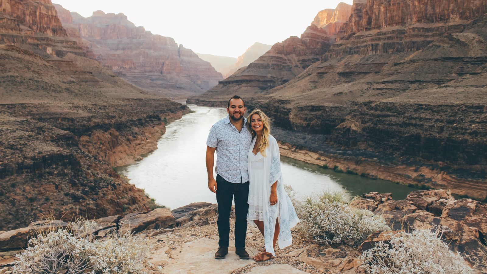 a man and woman pose together at the bottom of the Grand Canyon West at sunset