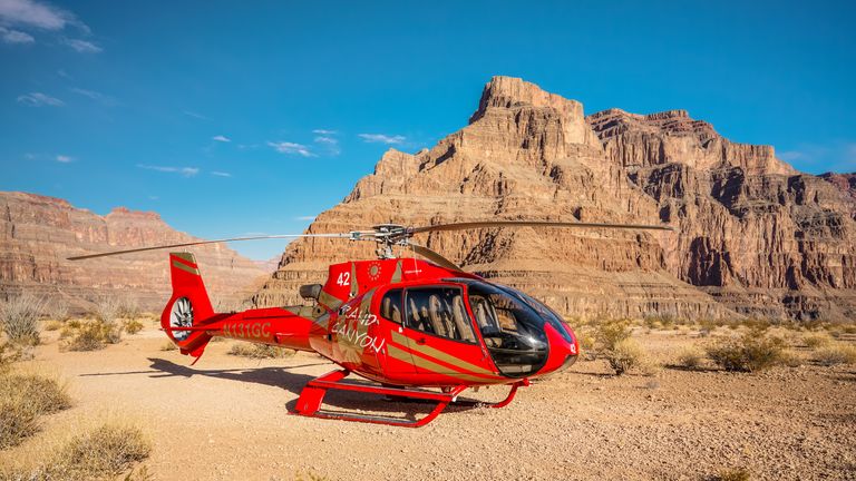 Red helicopter landed below the rim at Grand Canyon West with scenic backdrop.