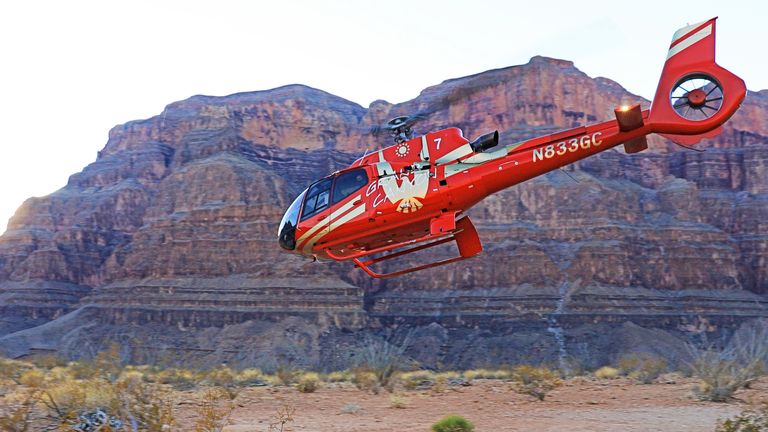 Red EC-130 helicopter taking off from the bottom of Grand Canyon