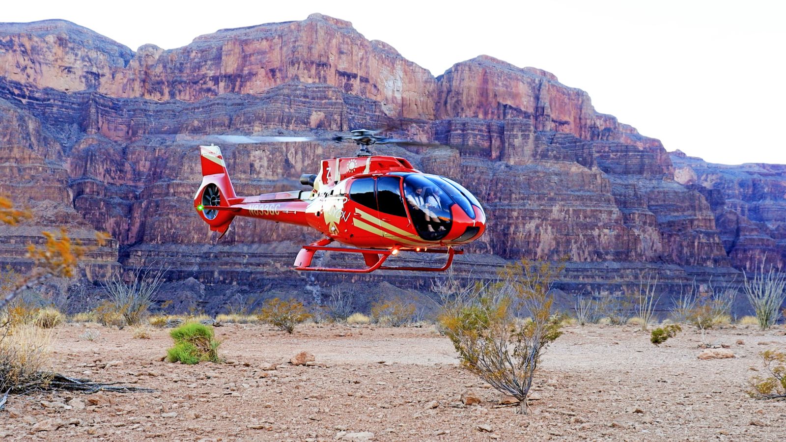 A Red EC130 Helicopter lifting off from the canyon floor at Grand Canyon West Rim
