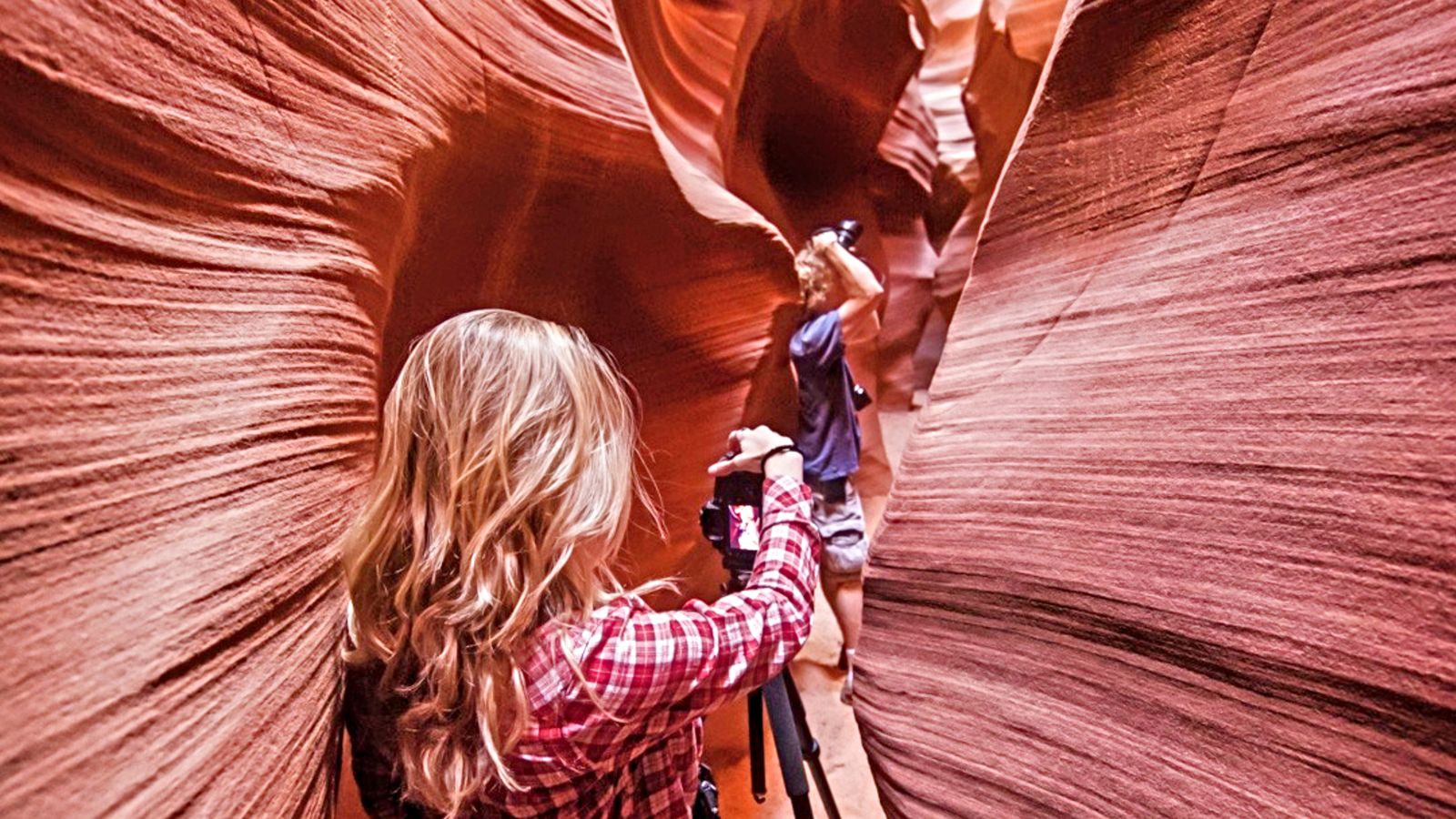 two guests on an Antelope Canyon tour take photos within a narrow sandstone corridor