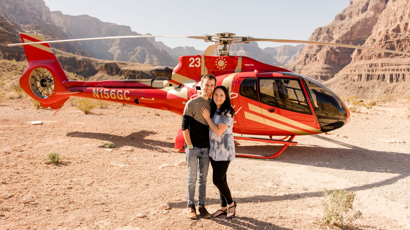 a couple stands next to a helicopter landed at the bottom of the Grand Canyon West