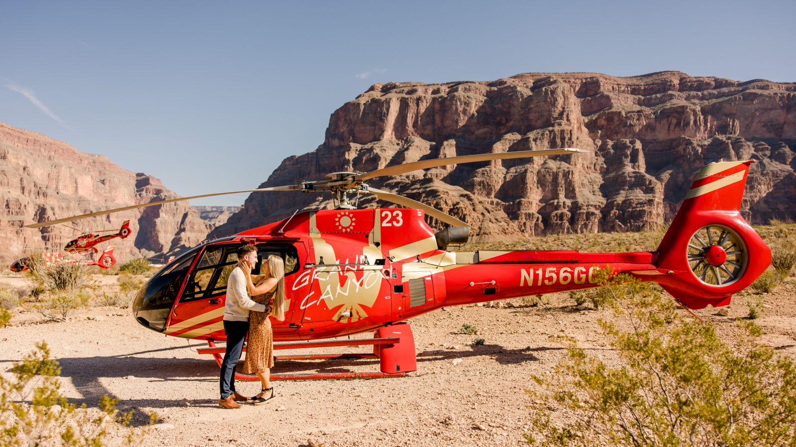 A couple standing in front of red helicopter at the bottom of the Grand Canyon.