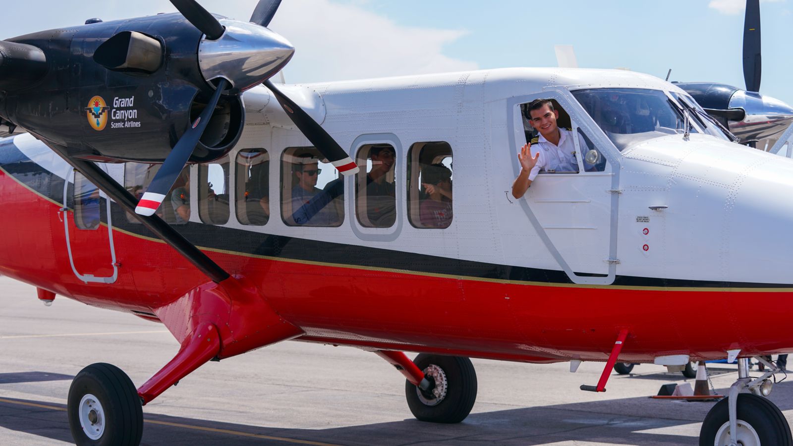 Airplane pilot waves as he prepares for takeoff with a group of passengers.
