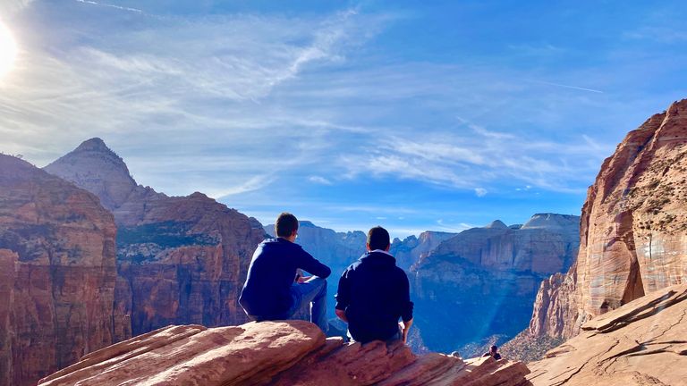 two men sit at the edge of a cliff at Zion National Park