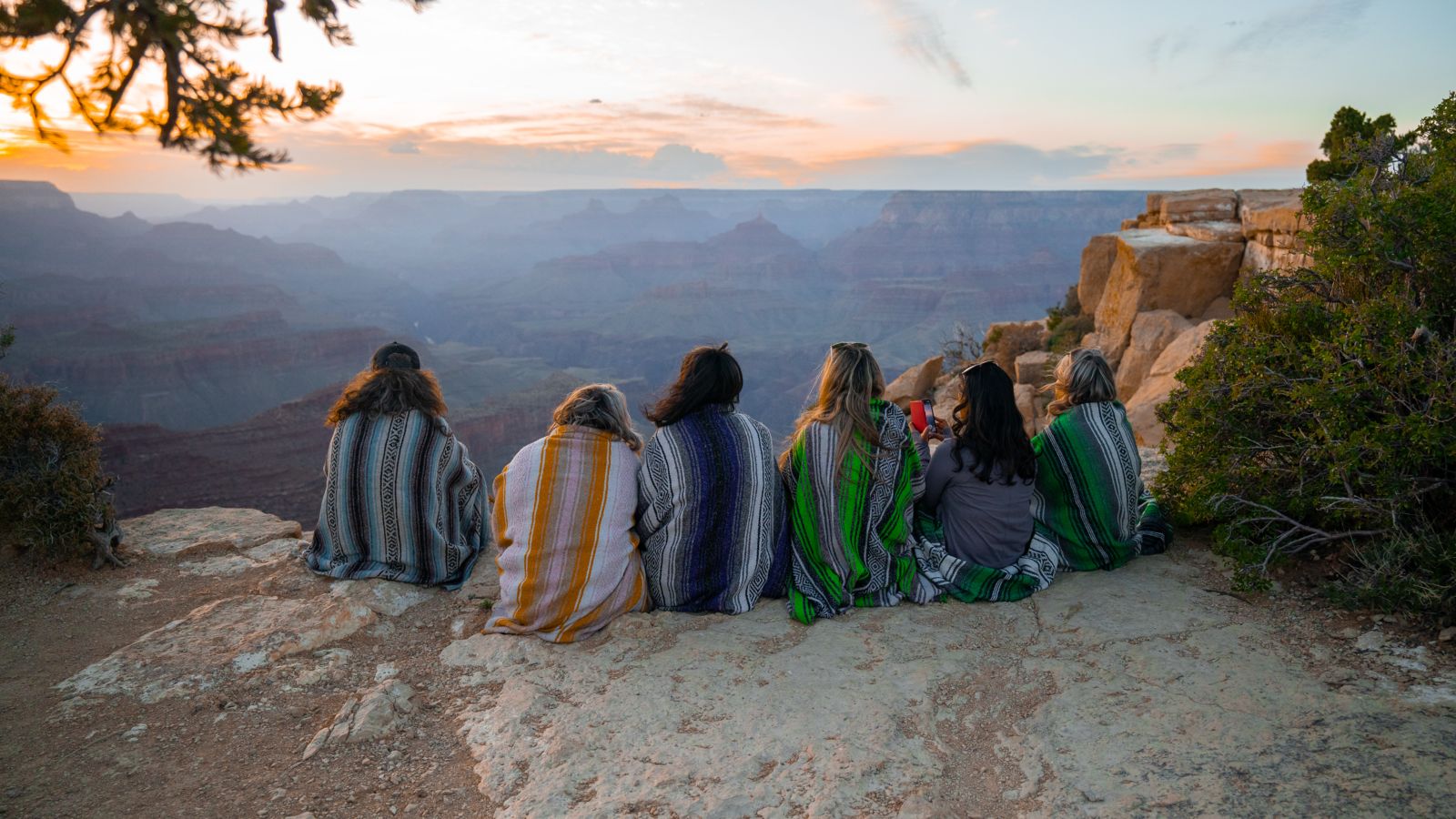 A group of people is sitting on the Grand Canyon's edge, viewing the sunset.