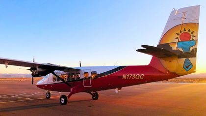 A Twin Otter airplane parked on the tarmac in front of the setting sun