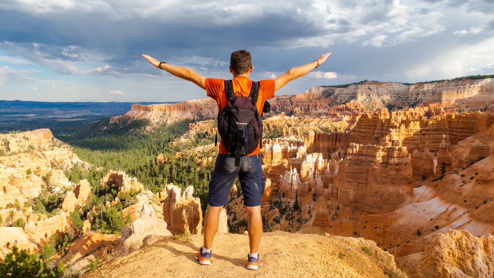 a man stands at the edge of a Bryce Canyon viewpoint with his arms in the air